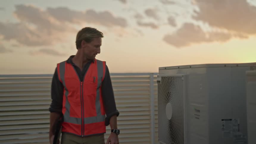 An employee walks past equipment on top of a building and glances as he passes by