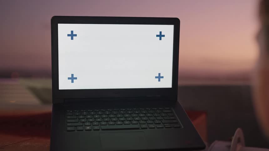 A man types on a laptop outdoors at sunset