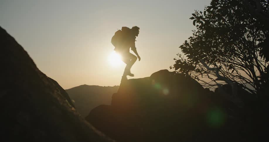 The sun shines brightly upon a man standing on rocks as he looks at mountains in the distance