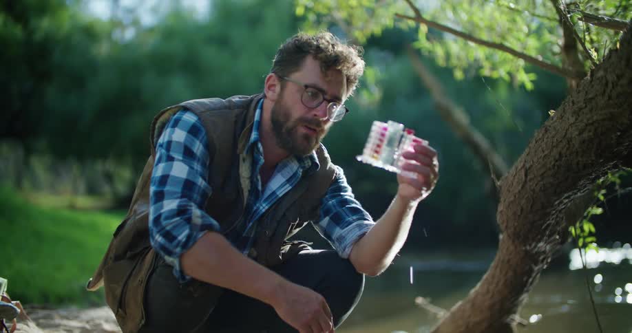 Man crouching near river takes a water sample