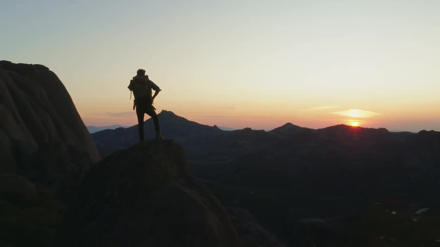 Person standing on a mountain peak watching the sunrise