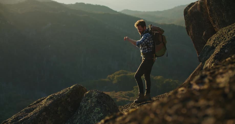 There is a young white man that is hiking on a cliff in the day time