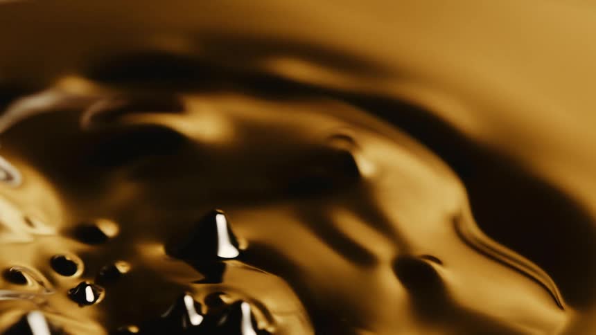 Surface of a shiny gold thick liquid disrupted by air bubbles flowing up