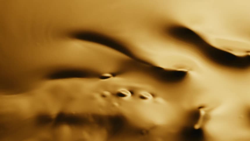 Light shines on a gold liquid substance as it ripples and moves