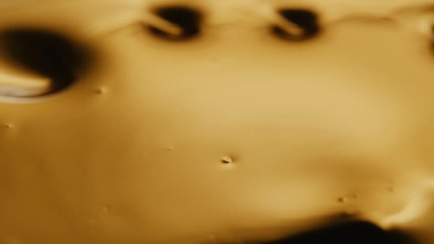 Light shines on a gold organic liquid substance and holes emerge as it ripples and moves