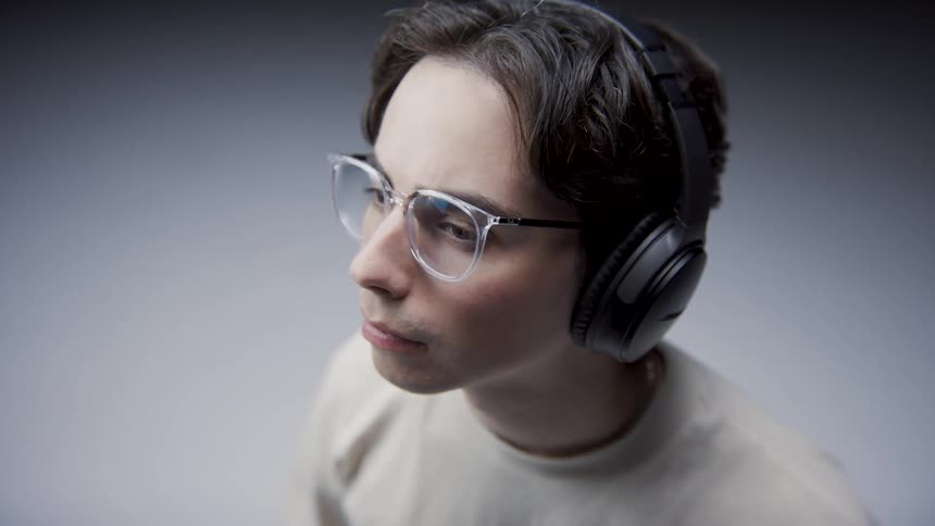 Man wearing headphones and eyeglasses looks upand around