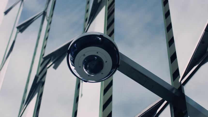 A small security camera is fixed to the outside of a tall building