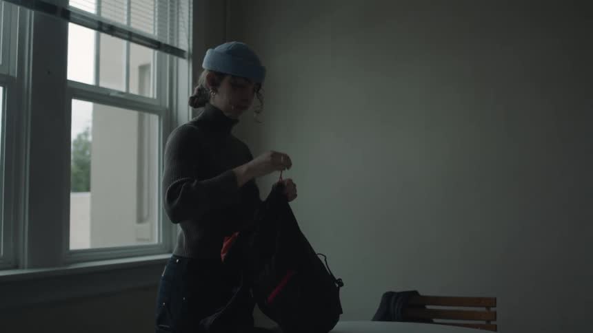Woman preps for hike and puts clothes in bag in her apartment
