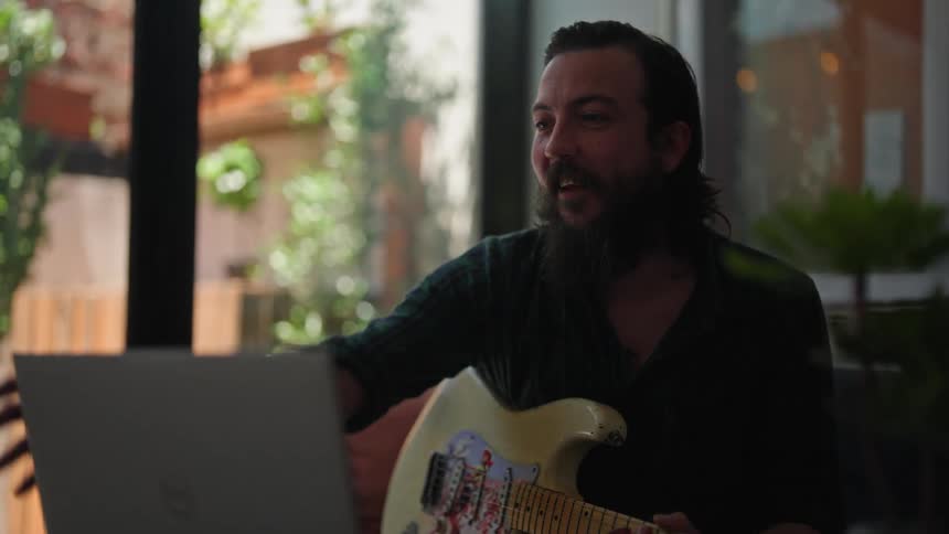 A man waves bye on video call then starts playing the guitar