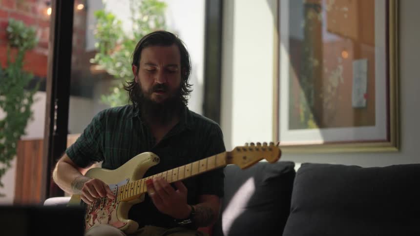 A man sitting on the couch strumming a guitar