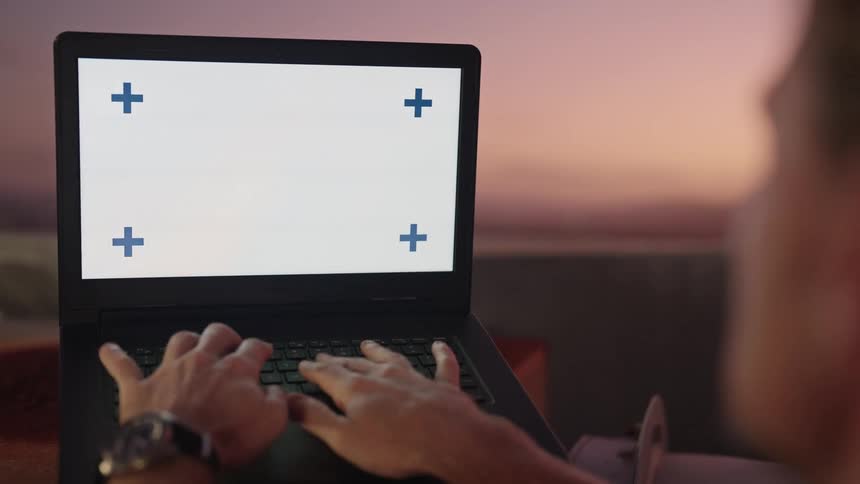Man typing on laptop working remote outdoors at the beach at sunrise