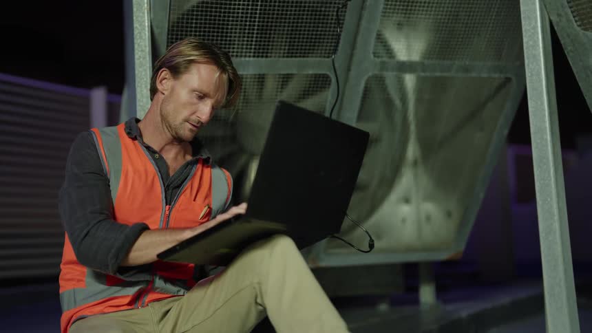 A man inspects and evaluates an exhaust fan atop a building