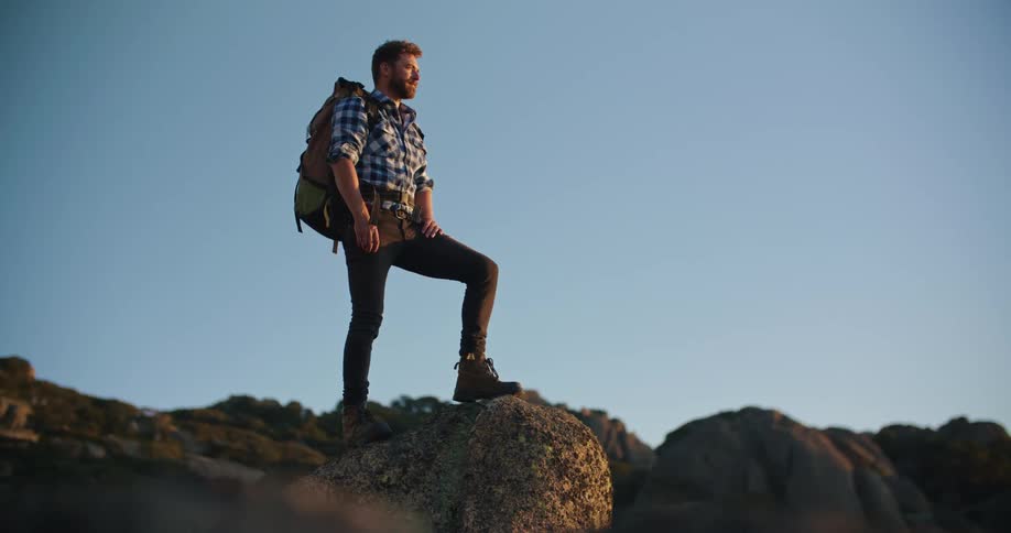 A young man is standing on a cliff and is hiking outdoors