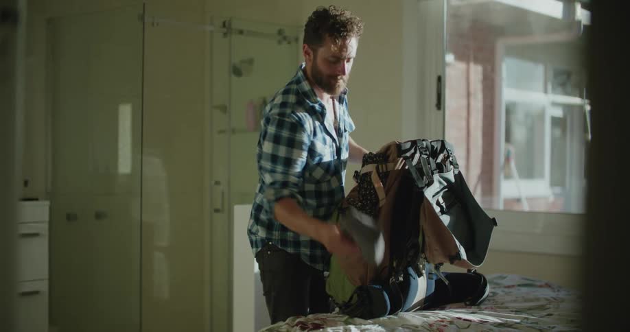 A young white man is packing inside of his room