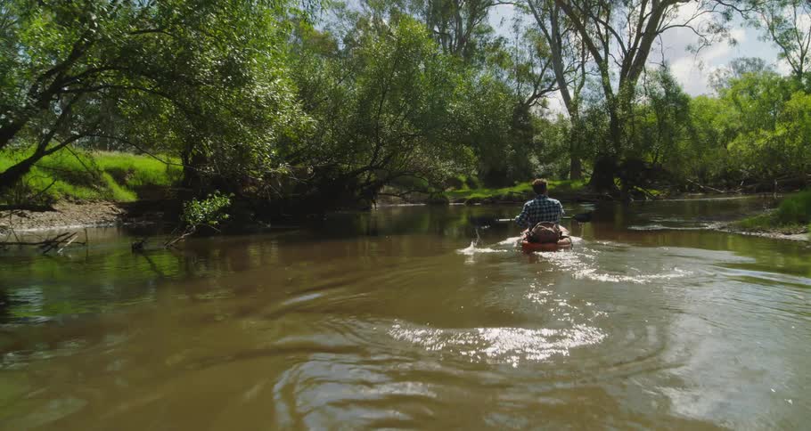 Following a man paddling a kayak on a gentle river in the countryside at daytime