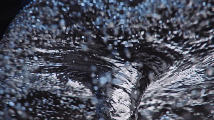 Light reflects on bubbles as they rotate around a swirling water vortex as it twists and turns