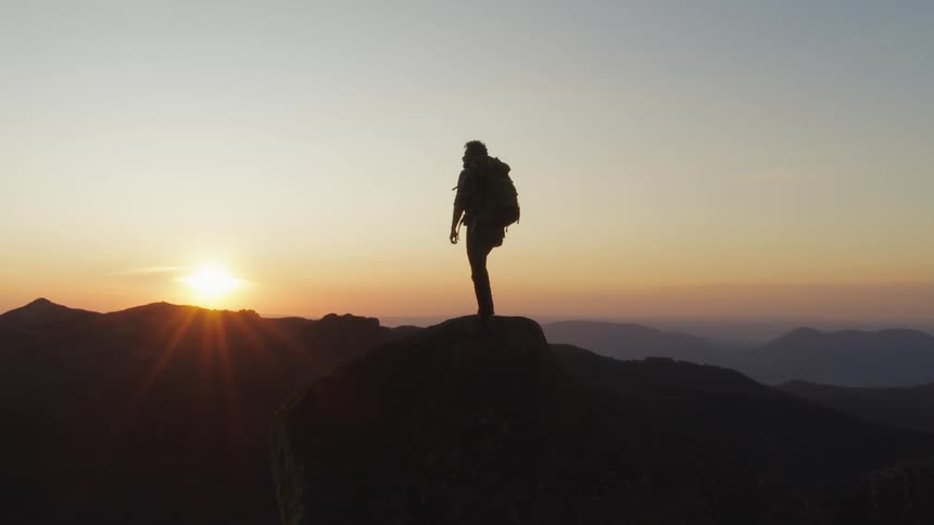 A hiker at dawn standing on top a mountain peak