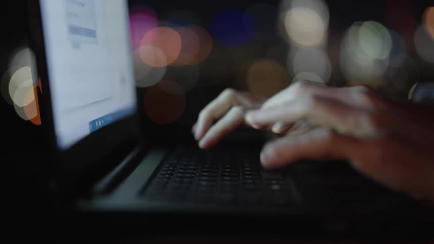A person typing on a laptop at night