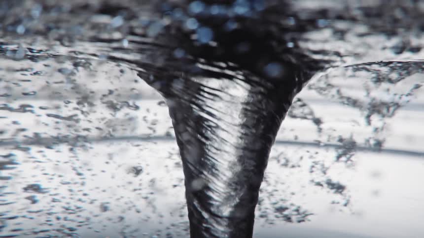 Light reflects on bubbles as they rotate around a swirling water vortex as it twists and turns