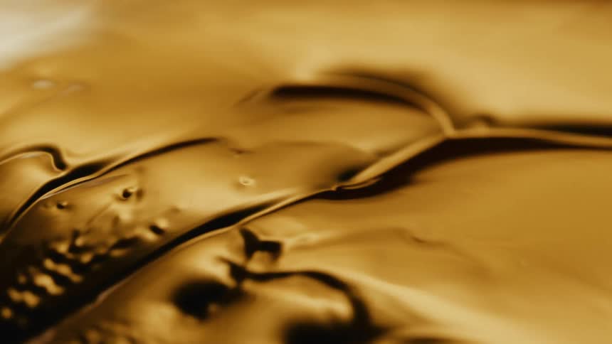 A gold liquid is moving and as it ripples a texture of bubbles and holes emerges from inside