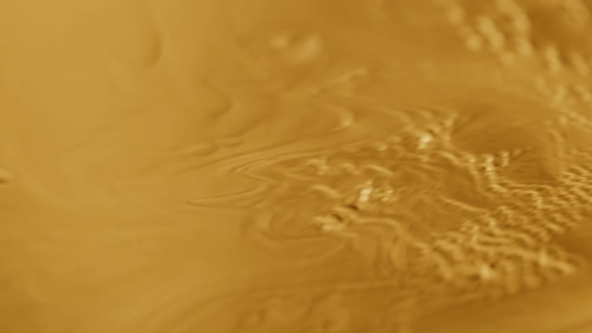 Gold metallic liquid is shown swirling around slowly and highly magnified