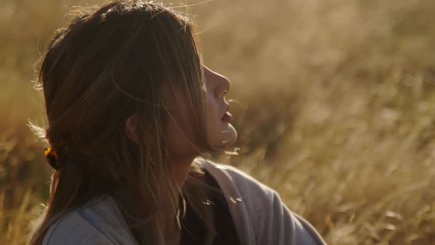 There is a young woman that is sitting down in a field of grass