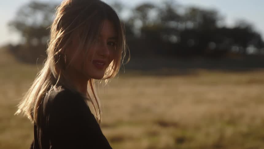 Woman with fair hair and black t shirt walks towards a clump of trees in the field
