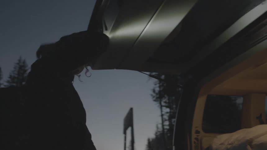 Woman grabs backpack out of her vehicle at dawn