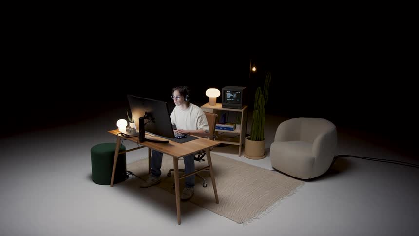 Man works on computer while sitting at desk in area occupying large empty dark room