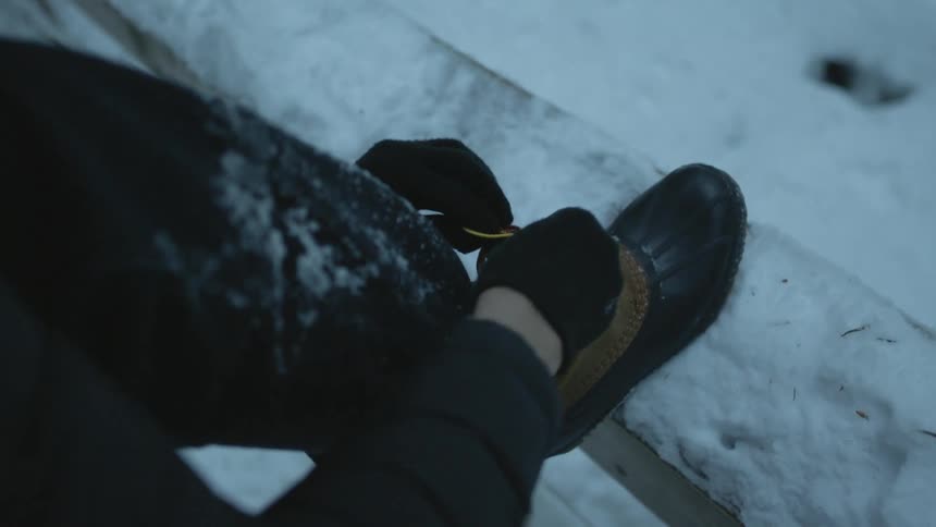 Person ties their boot while hiking in the snow