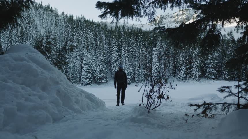 A person walks through a clearing in the trees across snow covered ground