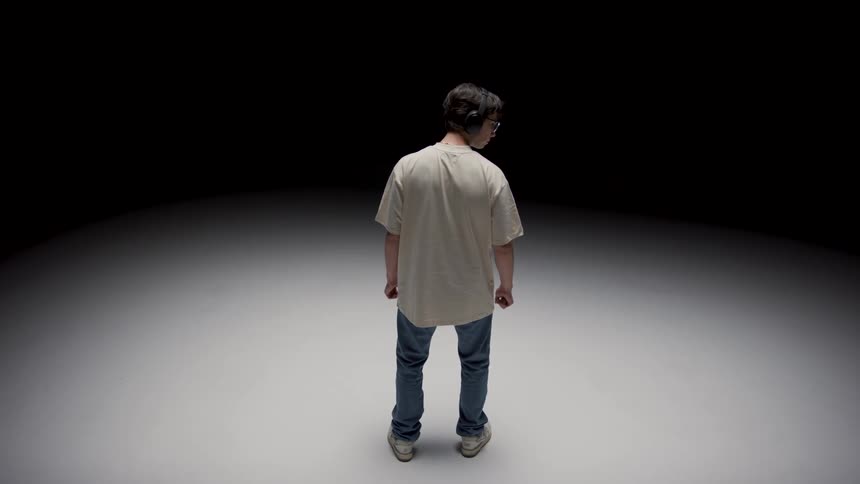 A man wearing headphones stands on a white floor that is orbiting slowly