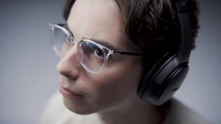 Close up of man wearing glasses headphones and white t shirt sitting at desk