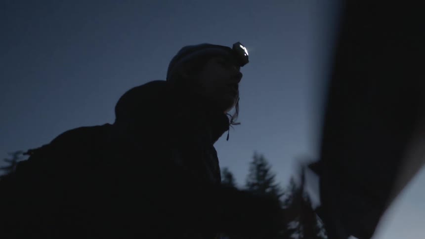 Woman wearing headlamp arrives at trailhead and hikes at dusk