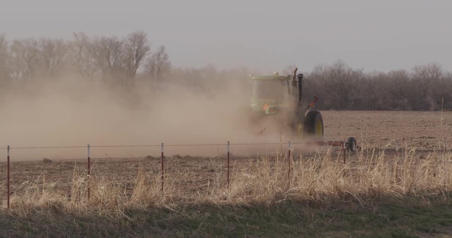 A tractor kicking up dust as it tills a field