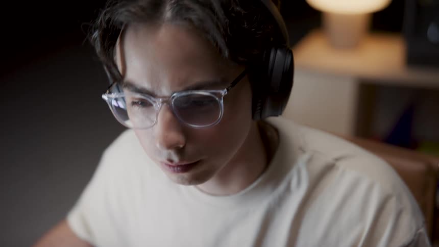 A young teenager is sitting down and playing on his computer