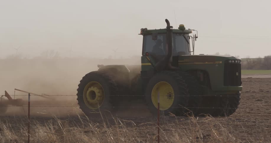A tractor tilling a field and kicking up dust