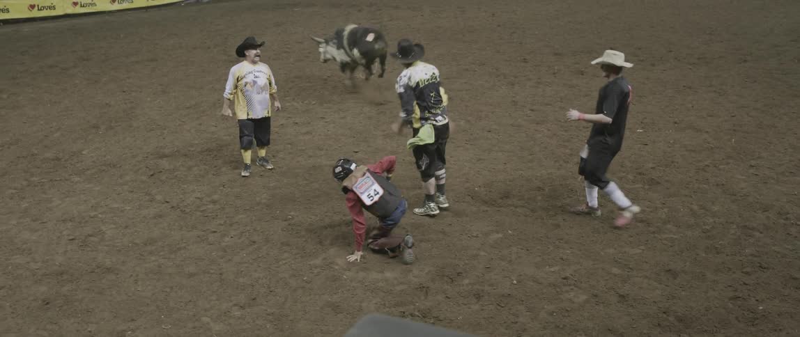 A man races out of a pen on a bull and falls off running back