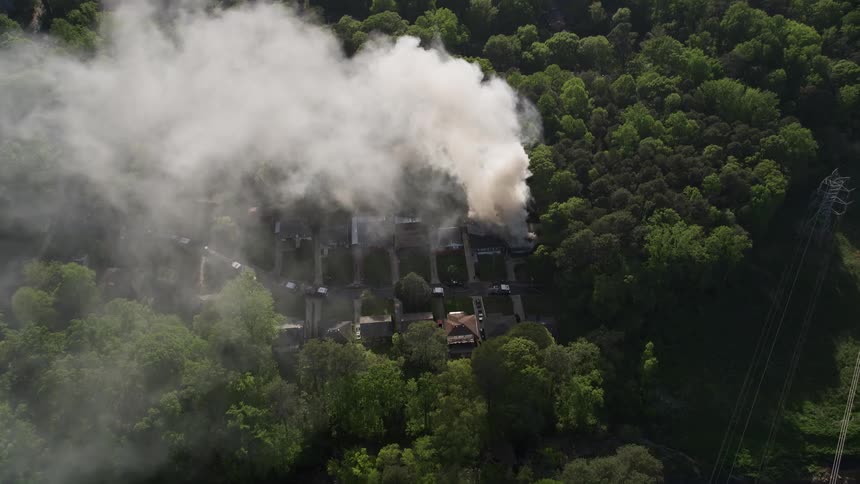 Aerial footage of a burning house in West Atlanta starting with a fly away from thick smoke then tilting to a birds eye view