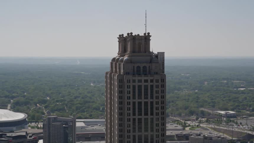 Aerial footage orbits the top of 191 Peachtree Tower in downtown Atlanta during a sunny day showcasing the high-rise supertall tower and the metropolis surrounding it