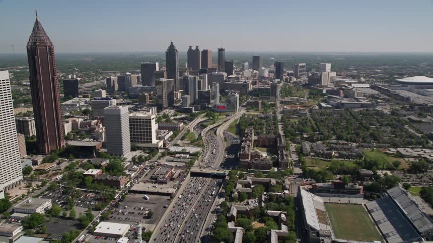 Aerial footage captures heavy traffic on the Downtown Connector heading towards Downtown Atlanta with tall skyscrapers overlooking the bustling metropolis
