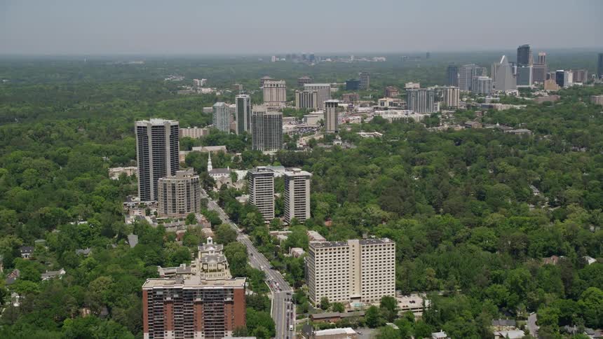 Aerial footage of Peachtree Road passing through the office buildings and wooded area of Buckhead Atlanta on a sunny day during spring or summer