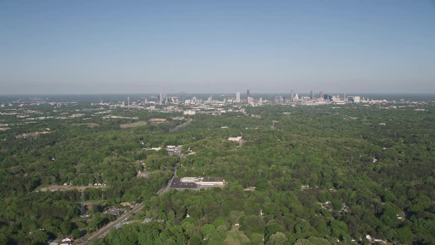 Aerial footage of Midtown Atlanta skyline is revealed after flying over a junkyard and dense forest