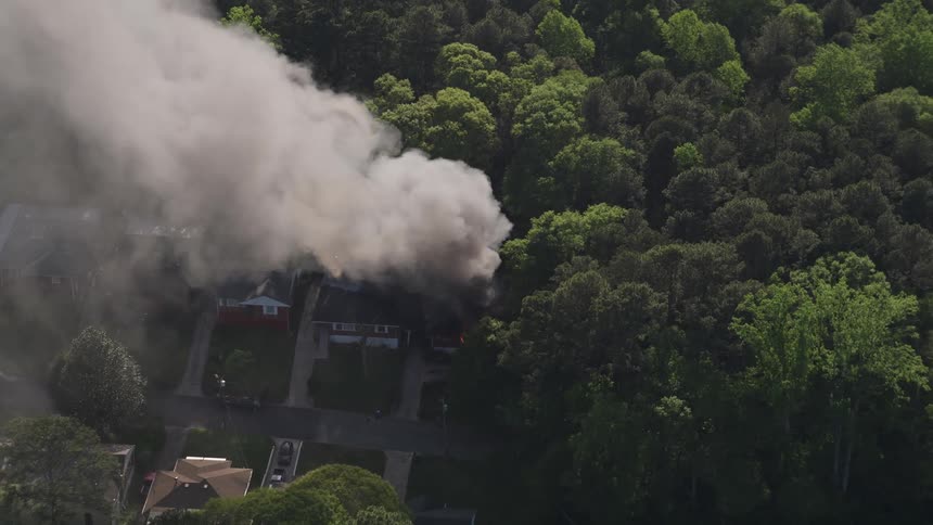Aerial footage of a burning home in West Atlanta Georgia with thick black smoke rising from the residential area