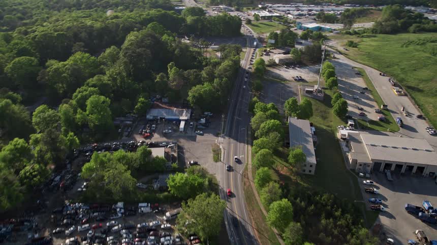Aerial footage captures vehicles driving on a parkway near an auto parts yard and trees in West Atlanta during daytime