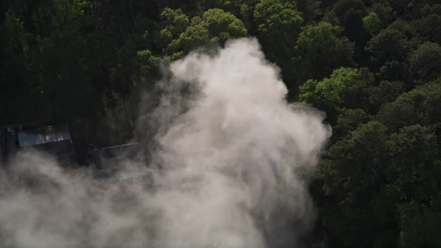 Aerial view of a house fire in a wooded area of West Atlanta with thick smoke rising