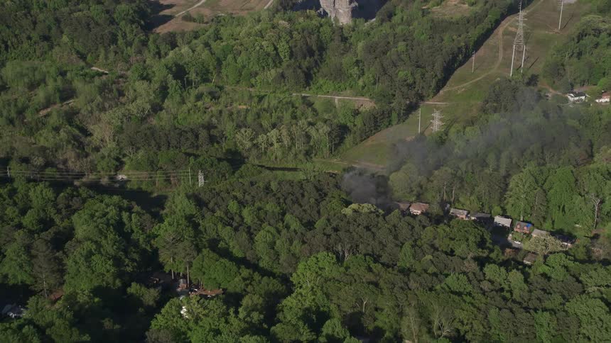 Aerial video footage of smoke rising from a house on fire in a wooded neighborhood in West Atlanta