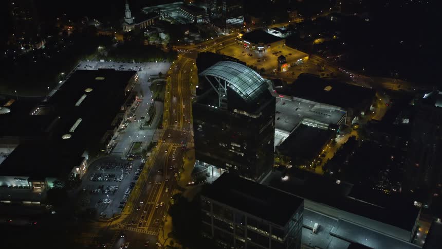 Approaching The Pinnacle in Buckhead Georgia at night the aerial stock footage tilts to birds eye view capturing the citys towers and skyscrapers glowing beneath a clear summer sky as traffic moves across downtown