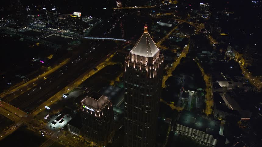 An aerial view of One Atlantic Center in Midtown Atlanta approached at night and tilting to a birds eye view of the glowing city skyline with tall brightly lit skyscrapers