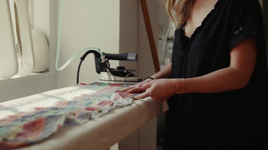 A woman lays a cloth down flat on an ironing board